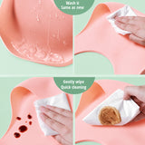Parent rinsing food off a waterproof silicone baby bib under a kitchen faucet.
