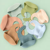Lightweight silicone baby bib rolled up compactly next to a diaper bag for travel convenience.